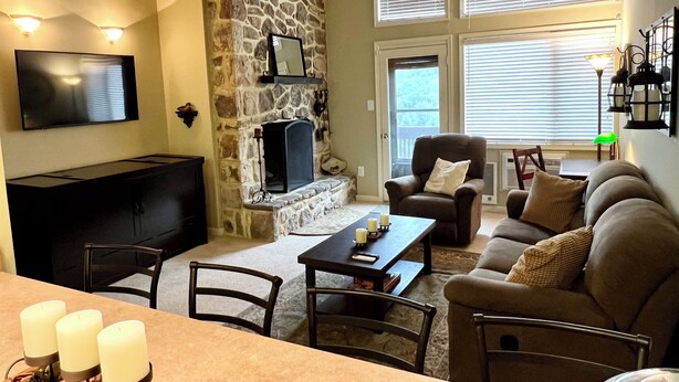 A cozy living room with a stone fireplace, a flat-screen TV, a comfortable sofa, and a dining area with candles.