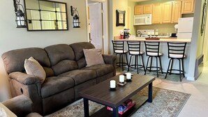 A living room with a brown sofa, a coffee table with candles, and a patterned rug.