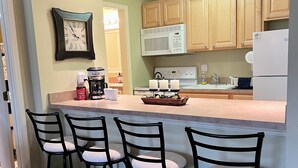 A kitchen with a central island, wooden cabinets, a microwave, a refrigerator, and a clock on the wall.