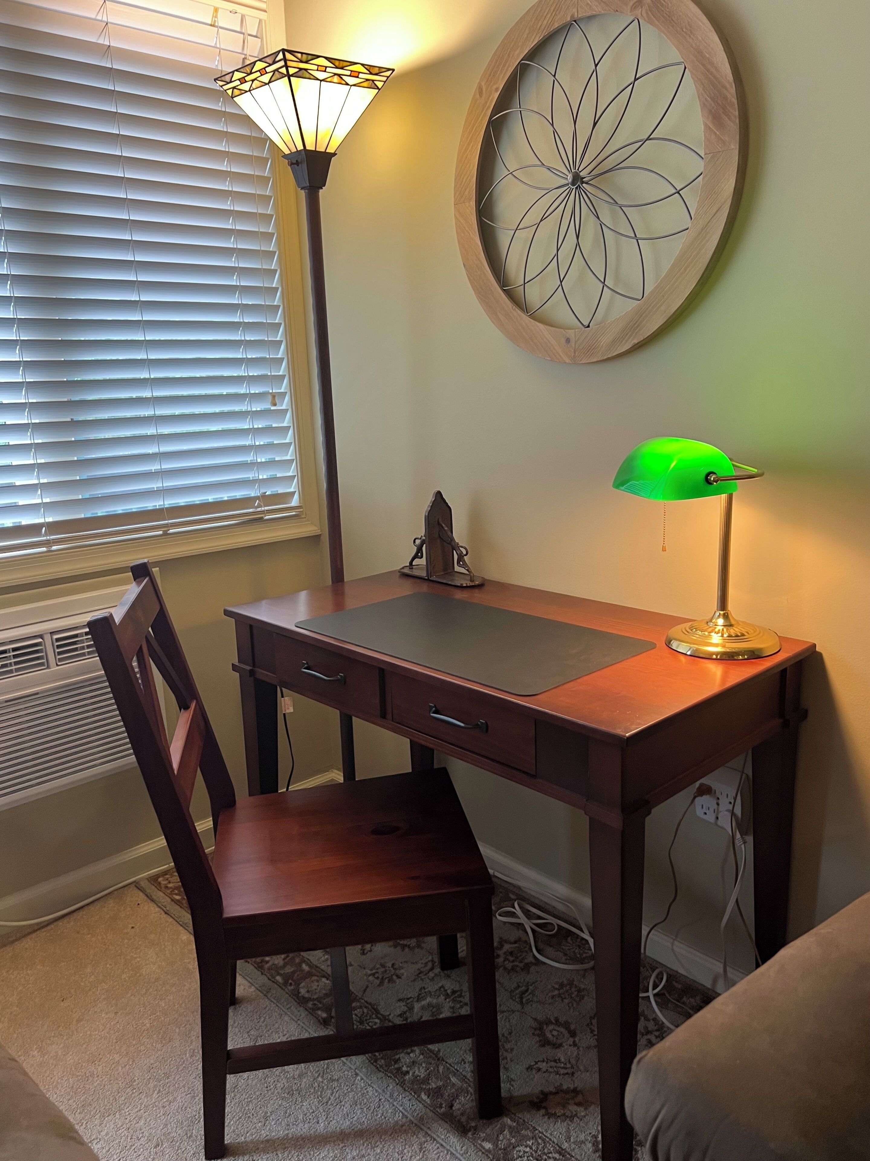 Un bureau en bois avec une chaise, une lampe de bureau verte et un élément décoratif fixé au mur.