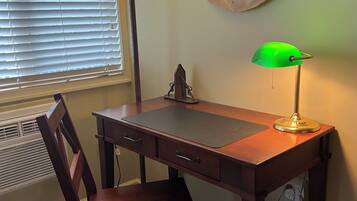 A wooden desk with a chair, a green desk lamp, and a wall-mounted decorative piece.