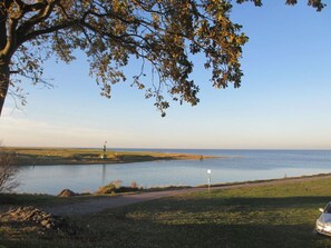 A lakeside view with a walking path, a lighthouse, and a car parked on the shore. - Haus Malerwinkel Comfortable Holiday Residence (Butjadingen)