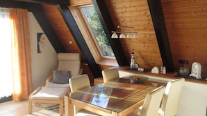 Un acogedor dormitorio en el ático con una mesa de comedor de cristal, sillas de madera, un banco acolchado y una pequeña cocina con una maqueta de faro.