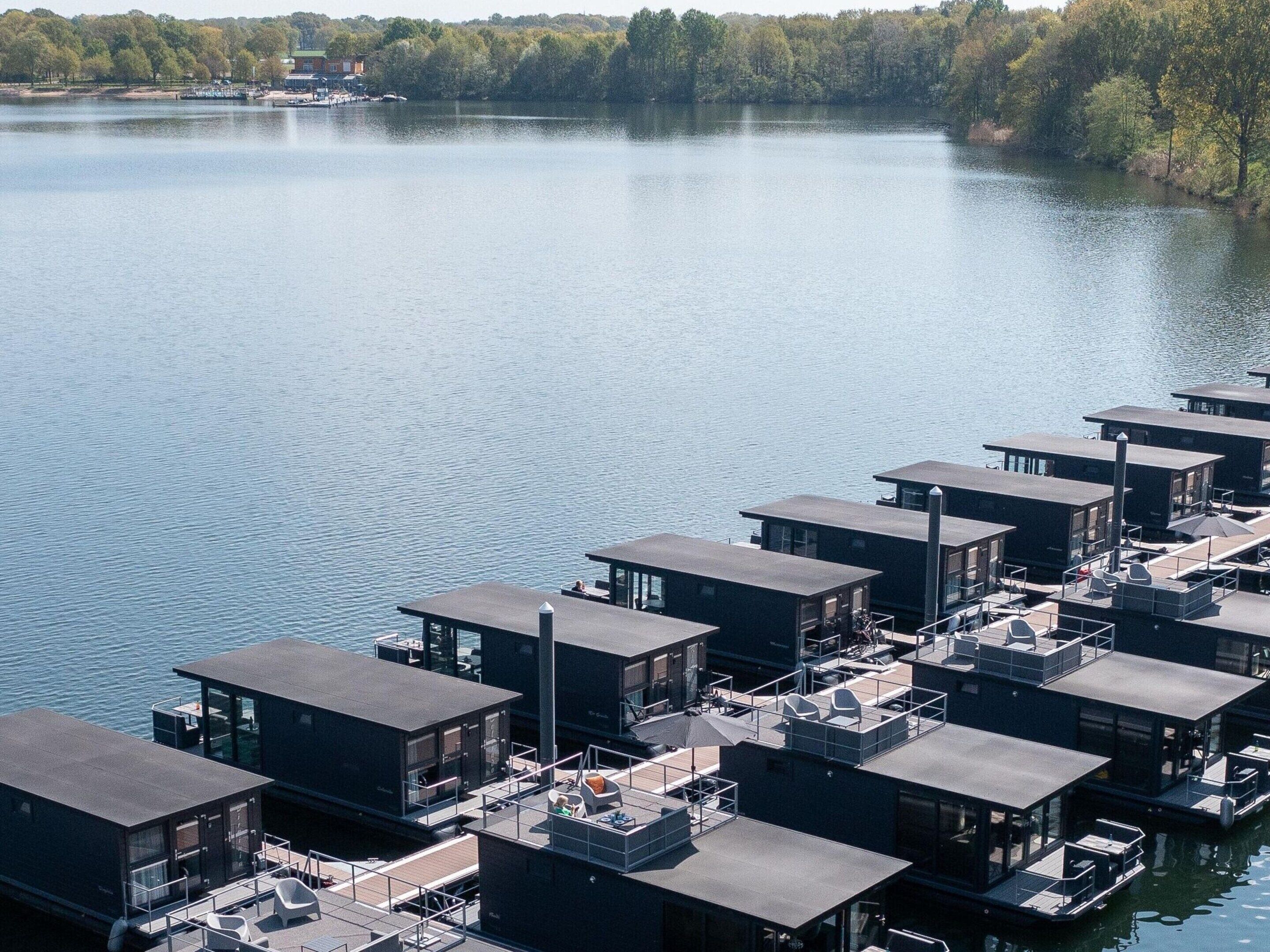 Une série de bâtiments modernes à structure flottante, dotés de façades en verre, disposés en rangée sur un lac paisible.
