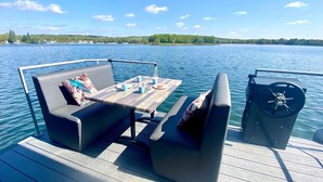 A deck with a table and seating, overlooking a calm lake with a distant shoreline. - Houseboat Mookerplas With a View (Middelaar)