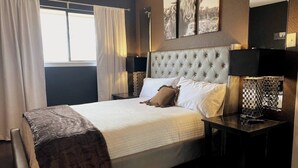 A neatly arranged bedroom with a large bed, a headboard, bedside tables, and a window with curtains.