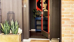 A modern entrance with a wooden door marked '4', a glass door with a red frame, a potted plant, and a blue shelving unit inside.