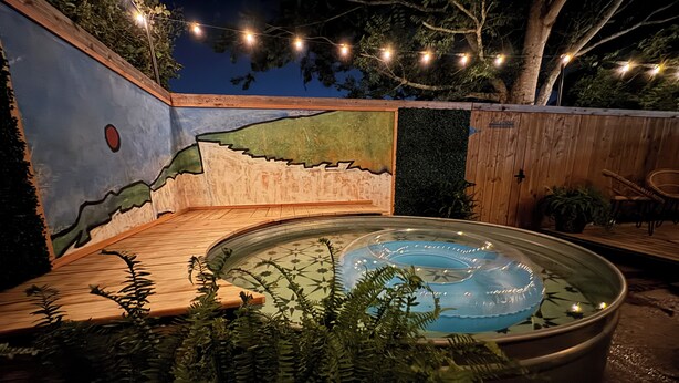 A hot tub with a wooden deck and a mural on the wall.