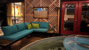 A modern living area with a teal sectional sofa, a wooden accent wall, a glass pool, and a red door.