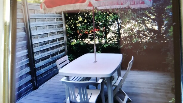 A patio with a white table and chairs, a red umbrella, and a wooden fence. - Le Moulleau Ctre, Front de Mer, Studio 2 Personnes Avec Terrasse (Arcachon)