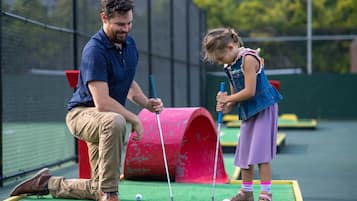 Un hombre y una niña joven jugando minigolf en un campo verde con un obstáculo rojo.