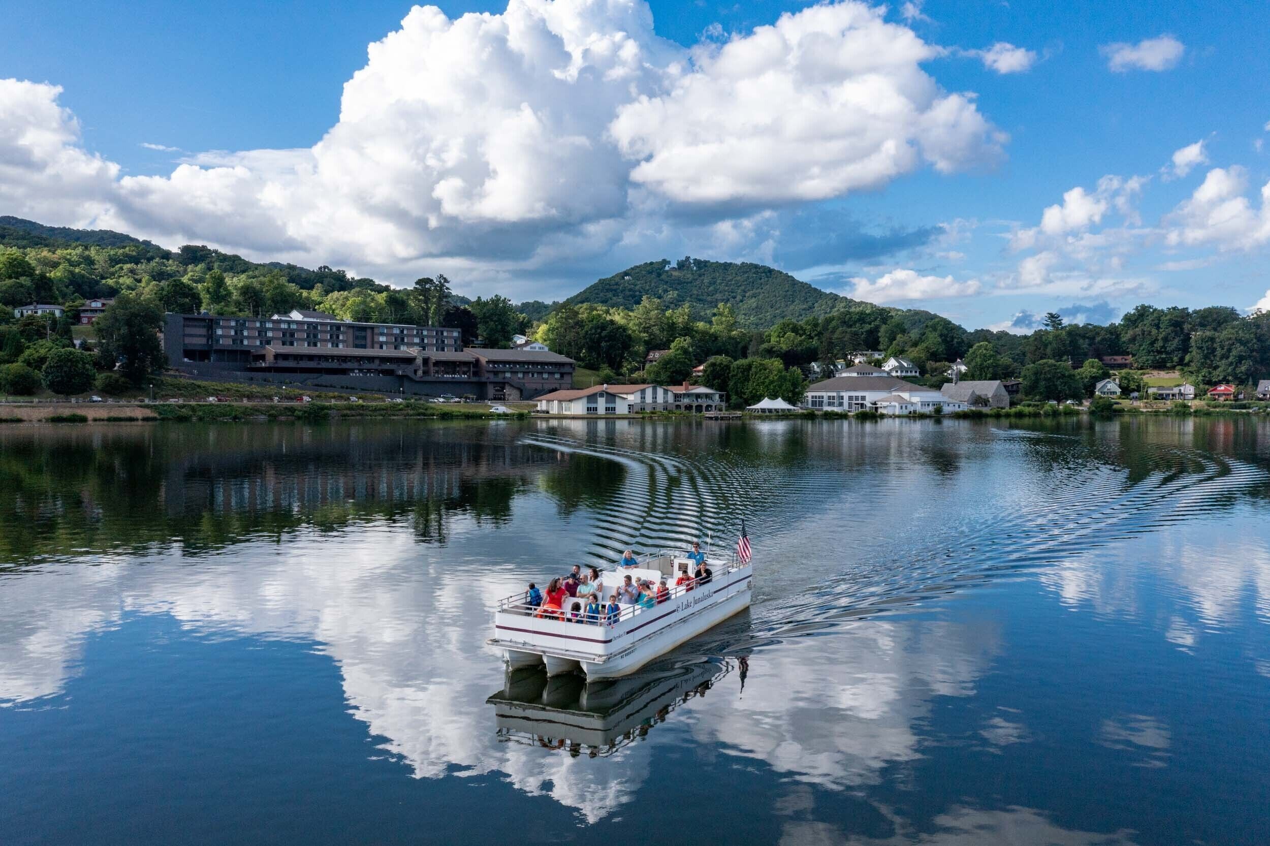 A boat with passengers on a calm lake, surrounded by buildings and greenery.