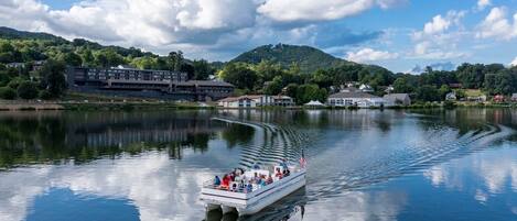 A boat with passengers on a calm lake, surrounded by buildings and greenery.
