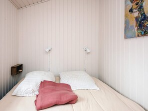 A bed with white bedding and a red pillow, two bedside lamps, and a small wooden shelf.