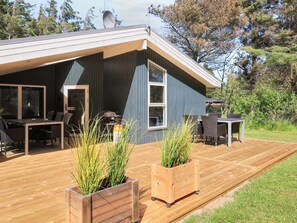 A modern house with a deck, outdoor furniture, and potted plants.