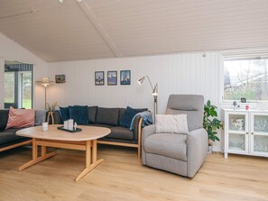 A modern living room with a grey sofa, a grey armchair, and a wooden coffee table. There are framed pictures on the wall, a floor lamp, and a cabinet with glass doors. - 8 Person Holiday Home in Lokken (Lokken)