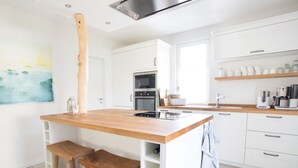 A modern kitchen with white cabinetry, a wooden island with stools, a built-in oven, and a coffee machine. - Holiday Home Reet-seaside (Glowe)