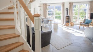 A spacious living area with a staircase, a fireplace, and a dining area with a view of the outdoors. - Holiday Home Reet-seaside (Glowe)
