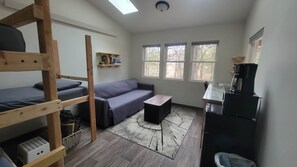 A compact room with a bunk bed, a sofa, a small table, a coffee machine, and a window with a view of trees. - Tiny Treehouse Cabin | Bluff Woodlands #3 (Elba)