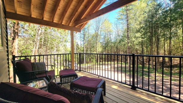 Une terrasse couverte avec des sièges extérieurs, entourée d’une zone boisée.