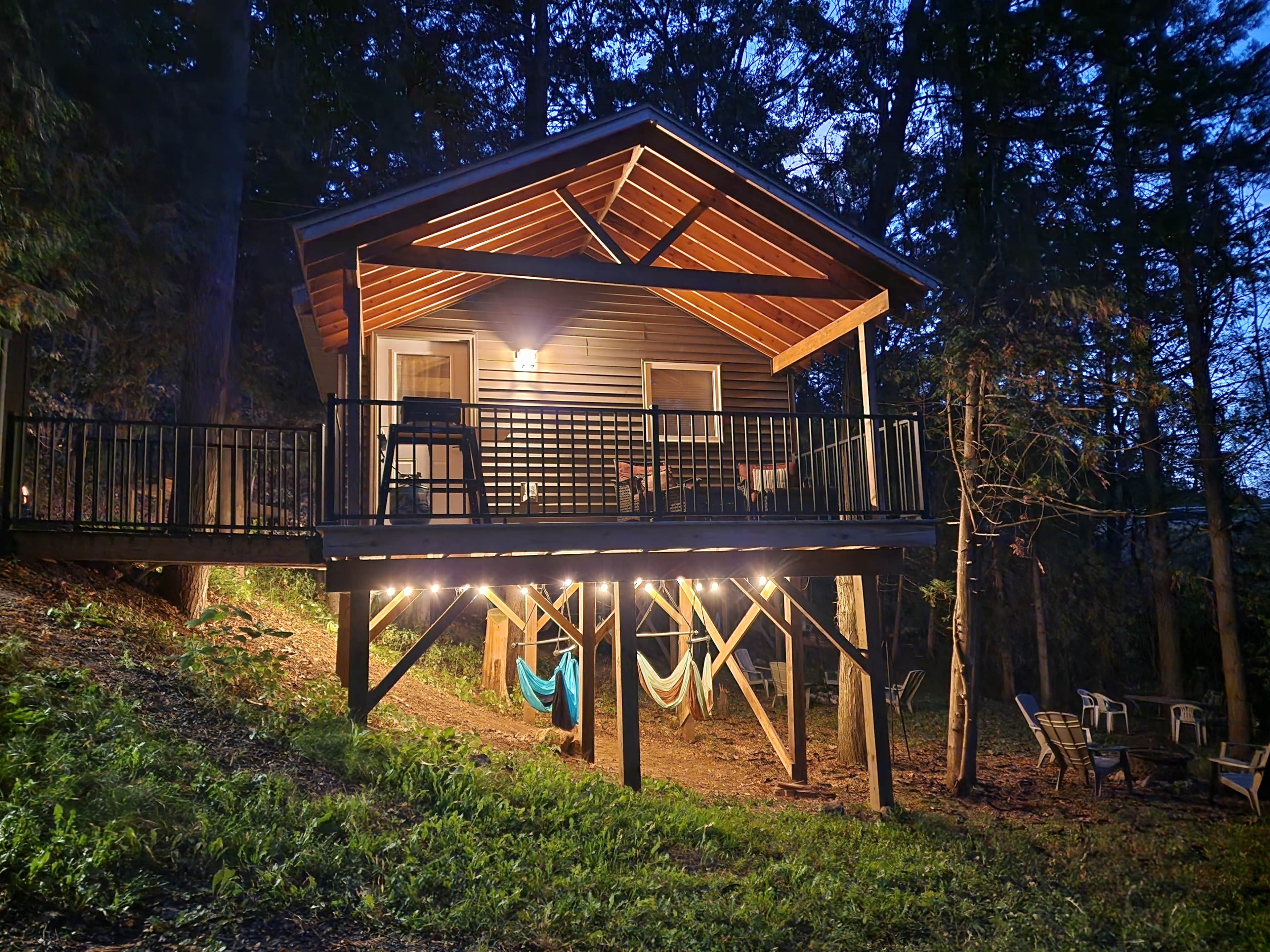 Una cabaña de madera con balcón, luces de adorno y mobiliario exterior.