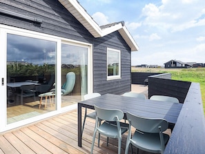 A deck with a table and chairs, a sliding glass door, and a view of the surrounding area. - 12 Person Holiday Home in Lokken (Lokken)