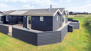 Ein modernes, dunkel gefärbtes Mobilheim mit überdachter Terrasse, Nummer 37, mit einer kleinen Holzterrasse und einer Eingangstür.