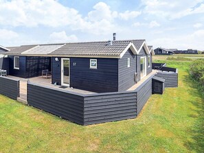 Ein modernes, dunkel gefärbtes Mobilheim mit überdachter Terrasse, Nummer 37, mit einer kleinen Holzterrasse und einer Eingangstür.