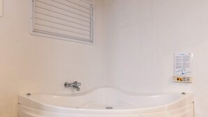 Eine weiße Badewanne in einem Badezimmer mit einer wandmontierten Bedienkonsole und einem Lüftungsgitter darüber.