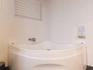 Eine weiße Badewanne in einem Badezimmer mit einer wandmontierten Bedienkonsole und einem Lüftungsgitter darüber.