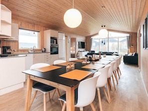 A modern kitchen with wooden cabinets, a dining area with a long table, and a living area with a sofa. - 12 Person Holiday Home in Lokken (Lokken)