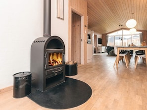 A modern interior with a wood-burning stove, a dining area, and a kitchen. - 12 Person Holiday Home in Lokken (Lokken)