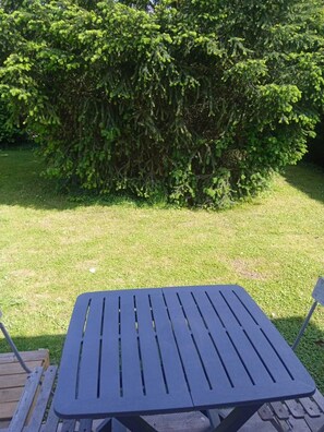 A square outdoor table with slatted sides, set on a grassy area with a dense green bush in the background. - 1 Bedroom Bed & breakfast in THORIGNY-SUR-OREUSE (THORIGNY-SUR-OREUSE)