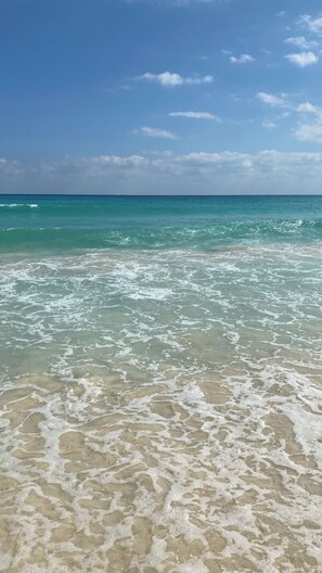 A beach with clear turquoise water and white foam on the shore.