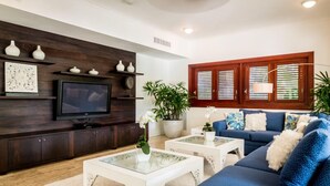 Ein Wohnzimmer mit einer Unterhaltungsanlage aus dunklem Holz, einem Flachbildfernseher, einem blauen Sofa und einem Couchtisch mit Glasplatte.