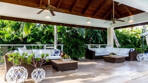 Ein Außenbereich mit Loungemöbeln aus Rattan, weißen Kissen und dekorativen Pflanzgefäßen.