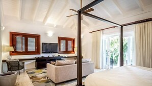 Ein Hotelzimmer mit Himmelbett, einer Couch, einem Schreibtisch mit Fernseher und einem Balkon mit Vorhängen.