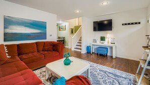 A living room with a red sofa, a white coffee table, and a blue vase. There is a staircase leading to another room.