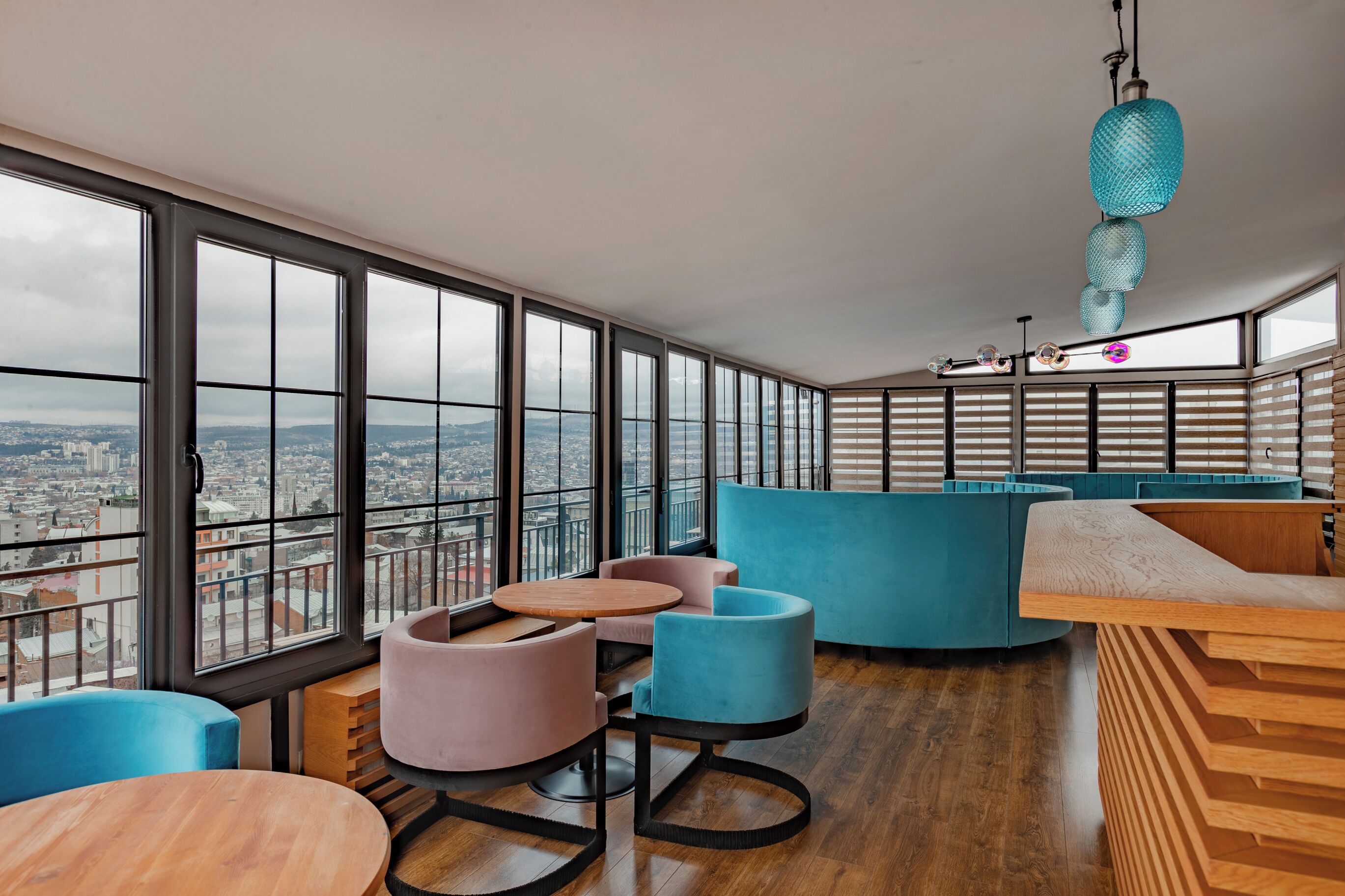 A high-rise interior with large windows, a wooden floor, and a mix of blue and pink seating.