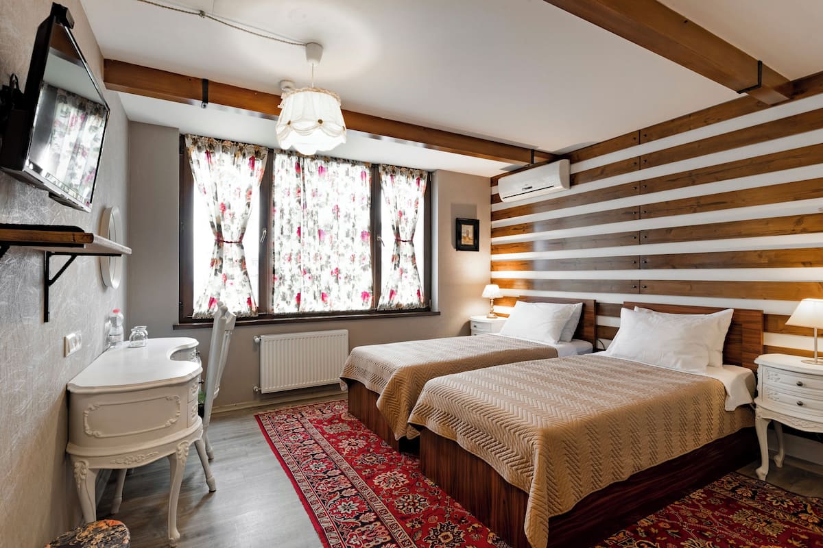 Een slaapkamer met twee bedden, een bureau, een stoel, een radiator en een raam met gordijnen.