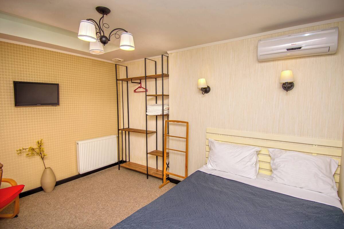 Hotelkamer met een bed, een televisie, een radiator, een wandplank en een luchtverkoeler aan de muur.