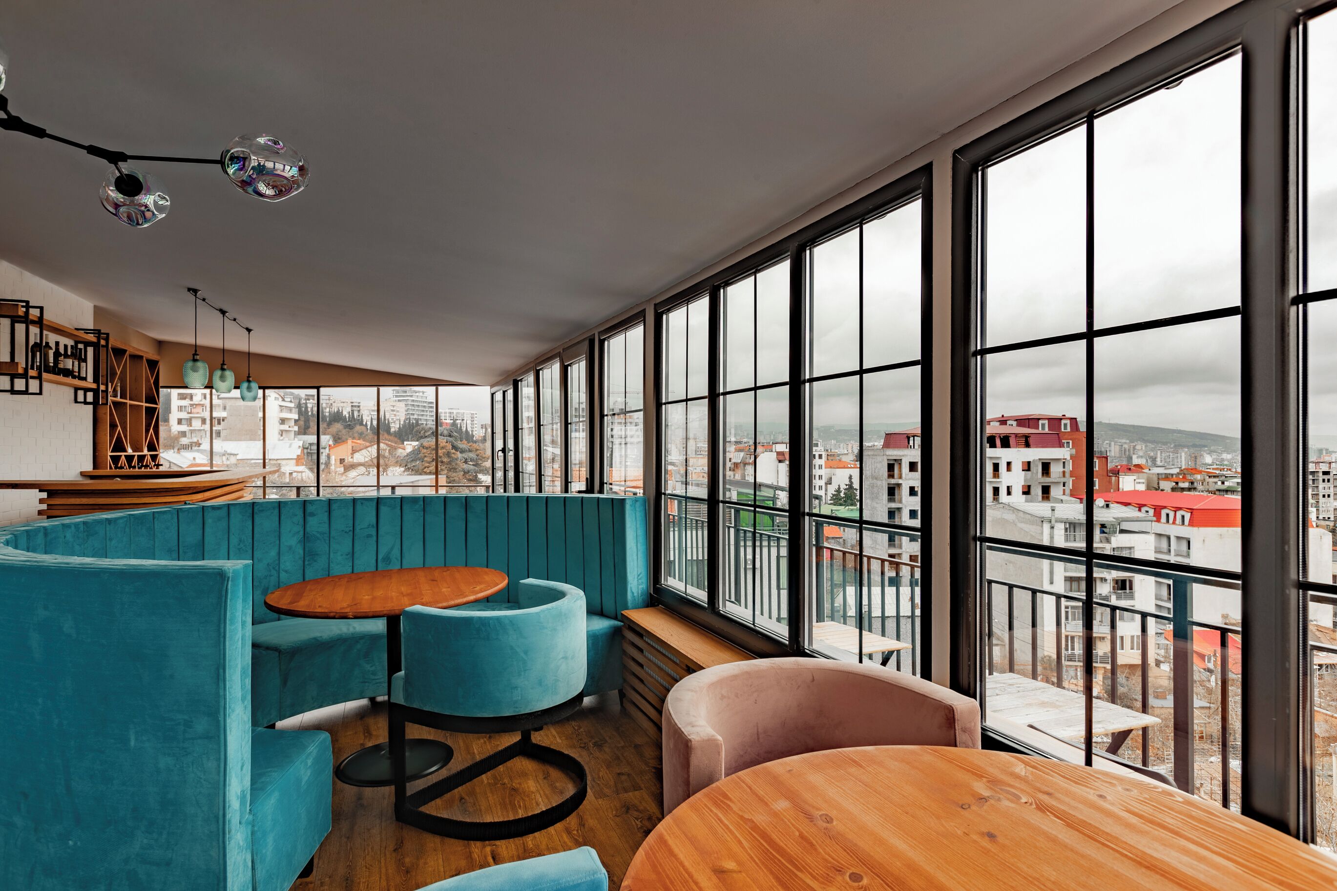 A modern interior with large windows, a wooden table, and teal seating.