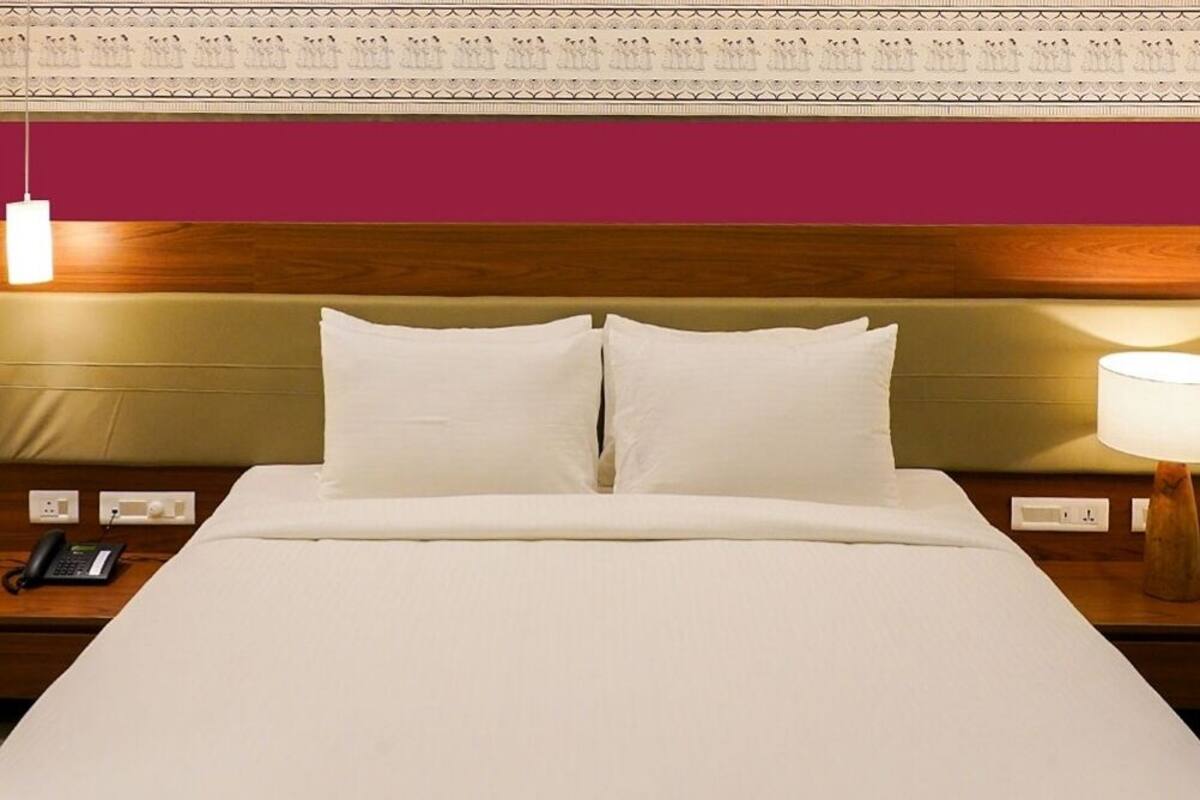 Una cama bien hecha con sábanas blancas, un cabecero de madera y una lámpara de noche.