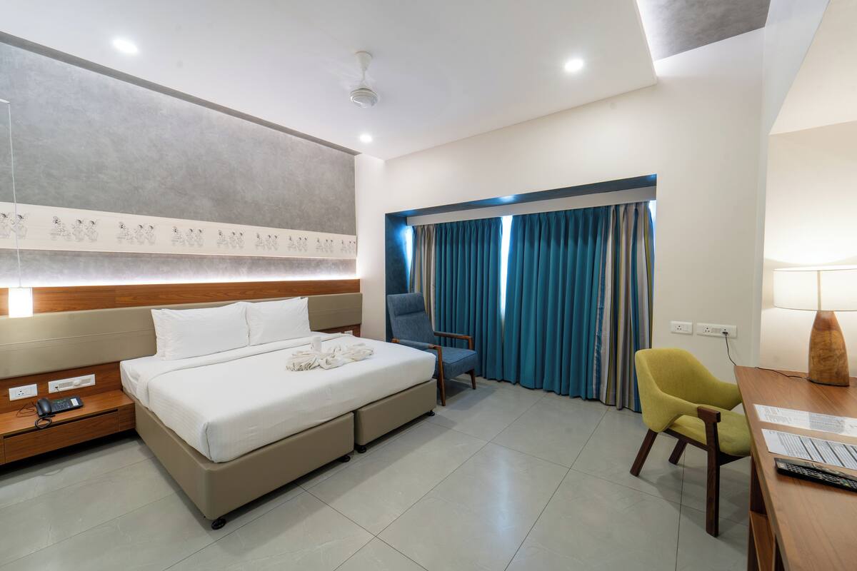 Habitación de hotel con cama, escritorio, silla y ventana con cortinas.