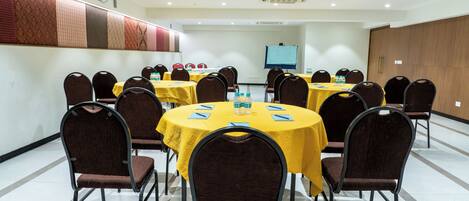 Sala de conferência com várias mesas e cadeiras, equipada com garrafas de água e cadernos.
