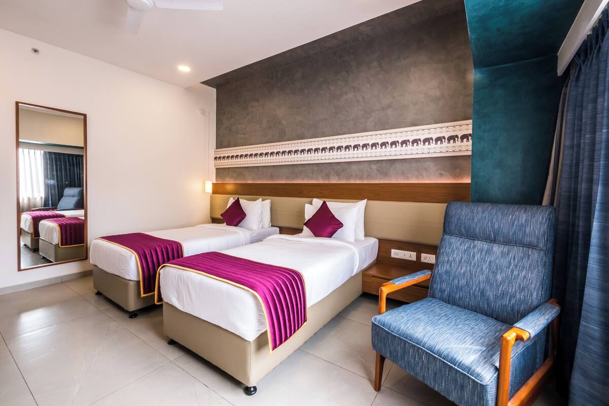 Habitación de hotel con dos camas, un espejo grande, un ventilador de techo y un sillón azul.
