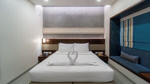 A hotel room with a neatly made bed, a bedside table with a phone, a nightstand with a lamp, and a built-in bench with a cushion.