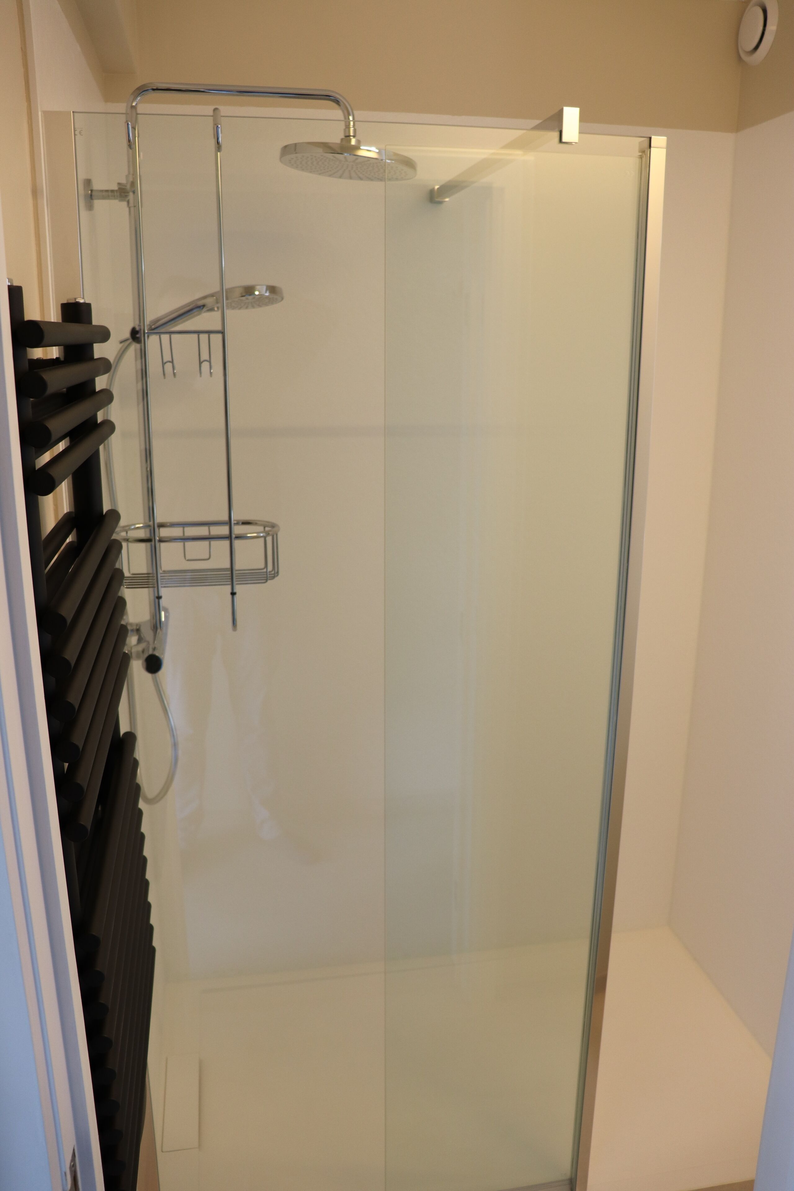 Eine Duschkabine mit Handbrause und am Wand montiertem Wasserhahn.