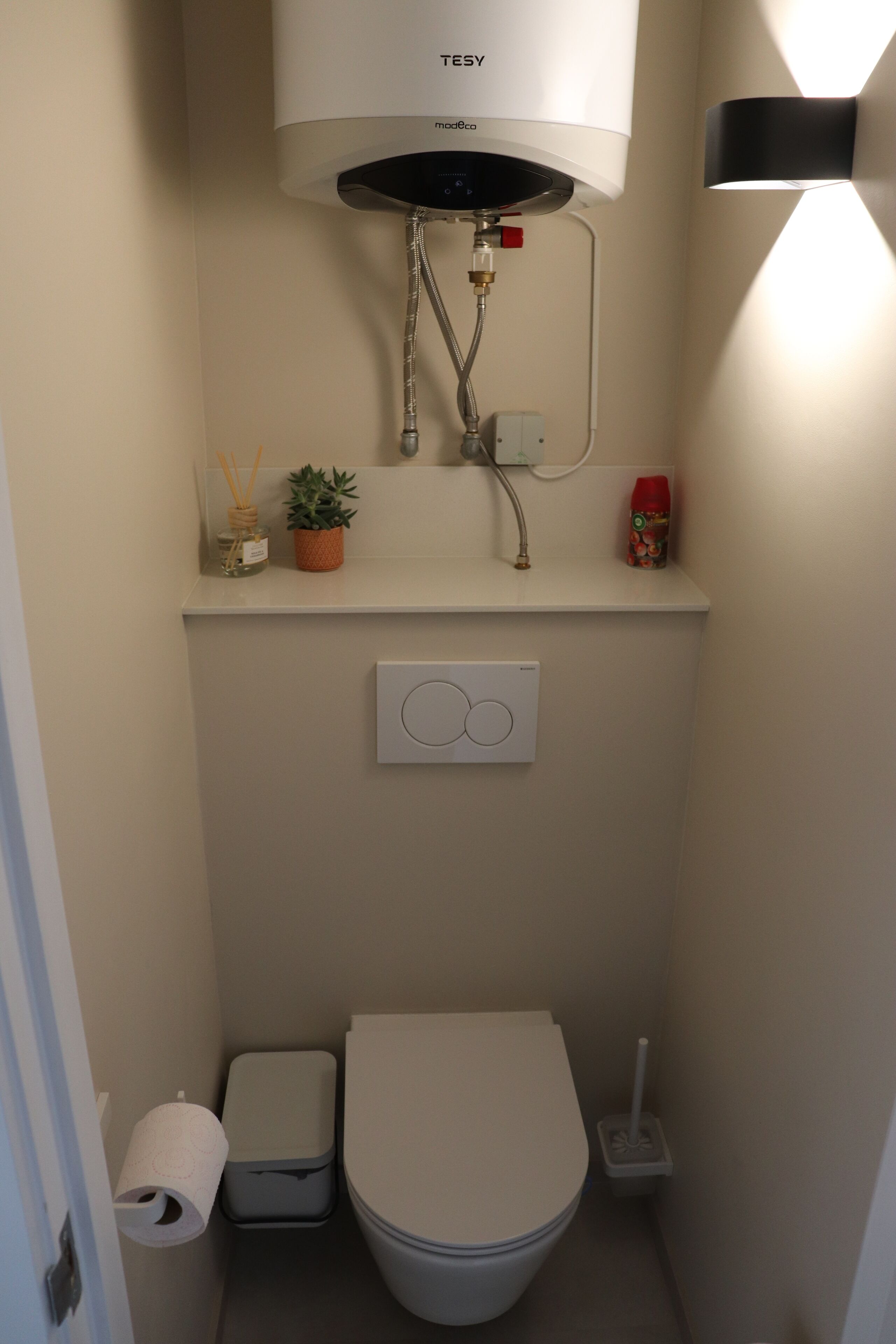 A compact bathroom with a toilet, bidet, and a water heater mounted above the sink.