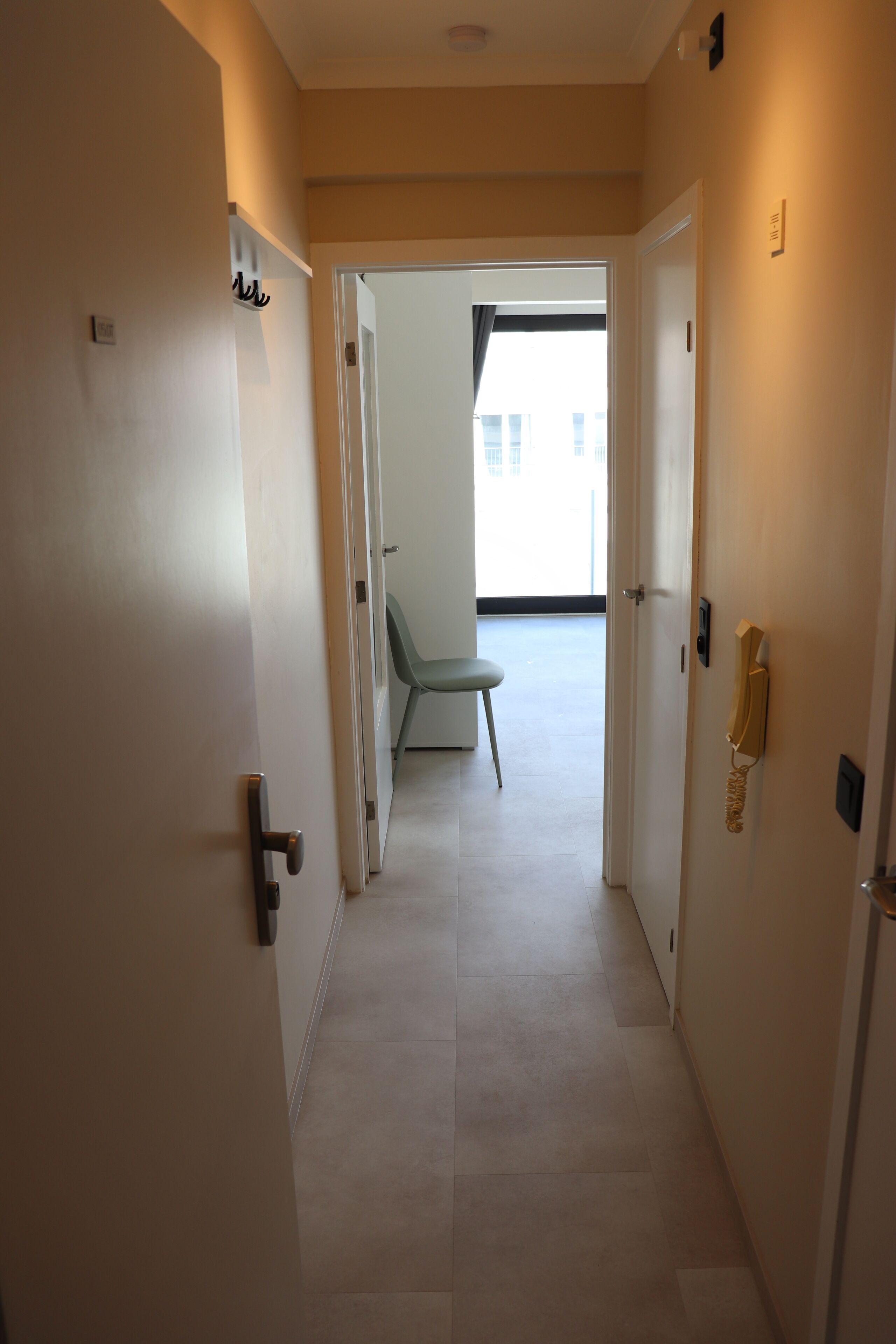 Un couloir avec une porte à gauche, une porte à droite et une chaise au centre.